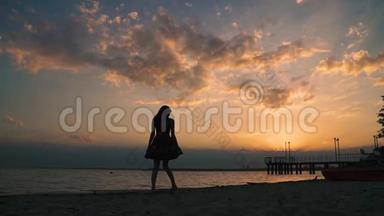 日落时海滩上一个穿着<strong>浅色</strong>连衣裙的女孩的剪影。 美丽的<strong>少女</strong>赤脚走在沙滩上。 慢动作
